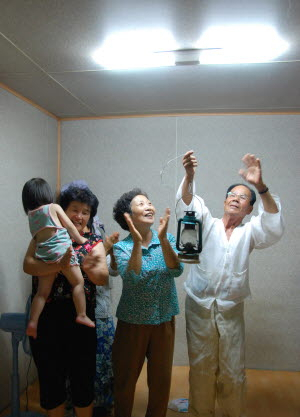 ▲ 이제형·안장수씨 노부부가 집 안방 형광등에 전깃불이 들어오자 이웃과 함께 환호하고 있다.