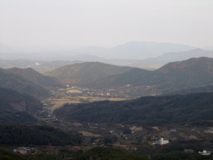 ▲ 팔공산 한티재에서 내려다 본 한밤마을. 북풍을 피해 산줄기가 다하는 곳에 마을이 자리 잡고 있다. 왼쪽 절벽에 군위 삼존석굴이 있다.