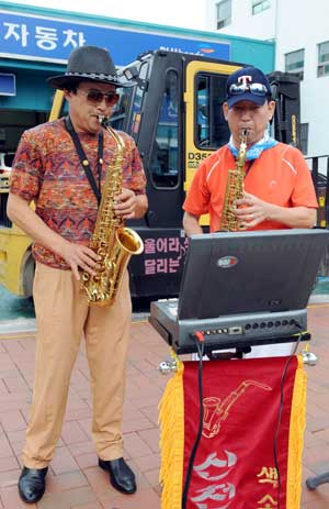 지게차 운전사 김상철(왼쪽)씨가 동료와 함께 대구시내 도로변에서 색소폰 연주를 하고 있다. 김태형기자 thkim21@msnet.co.kr