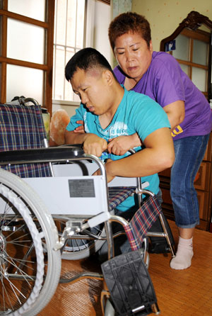 뇌병변 장애와 지적 장애를 갖고 있는 이상국(28) 씨가 휠체어에 오르기 위해 어머니 김금자(61) 씨와 혼신의 힘을 다하고 있다. 김 씨는 