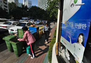 26일 오전 대구시 중구 남산동의 한 아파트 단지에서 주민이 음식물 쓰레기 수거통에 음식물 찌꺼기를 버리고 있다. 출입구 앞에는 음식물 쓰레기 줄이기 홍보용 포스터가 나붙어 있다. 우태욱기자 woo@msnet.co.kr