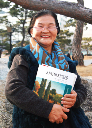 일흔셋의 나이로 대구보건대학교에 입학한 김복례 할머니가 대학교정에서 교재를 품에 안고 활짝 웃고 있다.