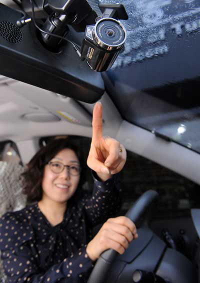 한 여성 운전자가 자신과 자신의 차량을 지켜줄 블랙박스를 보며 든든한 표정을 짓고 있다.