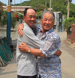 경북도 울진군 나곡6리 임명철(왼쪽)이장과 강원도 삼척시 월촌2리 김광웅 이장이 각각 울진과 삼척 쪽 가정집을 배경으로 도 경계선인 마을 한복판 소도로에서 포옹을 하며 우의를 다지고 있다.