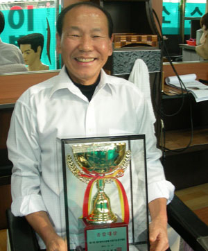 53년간 이용인 생활을 해온 임광택 씨가 자신의 이용소에서 제21회 대구시장배 이용기능경기대회 종합대상 트로피를 들고 활짝 웃고 있다.