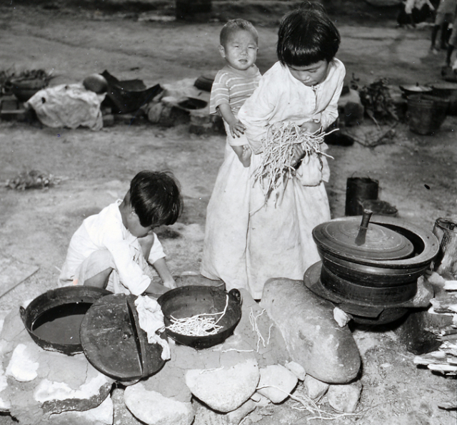 1951년 8월 18일 피난민촌에서 먹을 것이 없어 풀뿌리로 밥을 짓고 있는 어린 소녀