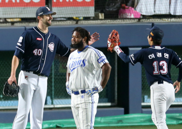 27일 대구시민야구장에서 열린 2015 한국시리즈 2차전 두산 베어스 대 삼성 라이온즈 경기. 두산 투수 니퍼트가 6회 말을 무실점으로 막은 후 더그아웃으로 들어오는 허경민과 하이파이브를 하는 가운데 삼성 나바로가 허탈한 표정을 짓고 있다. 연합뉴스