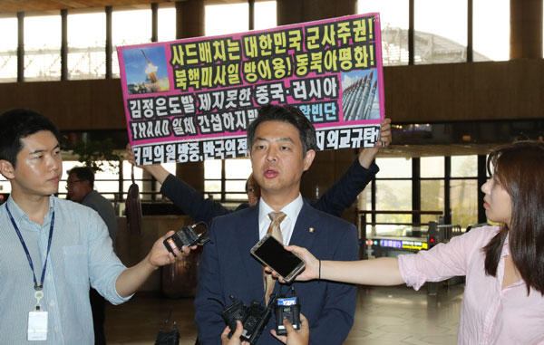 한 사회단체 회원이 8일 오전 김포공항에서 사드 관련 중국 방문에 앞서 기자들과 인터뷰하는 더불어민주당 김영호 의원 뒤에서 더민주 초선 의원들의 방중에 반대하는 현수막을 펼치고 있다. 연합뉴스