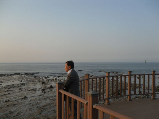 김일광 작가가 해가 지는 영일만을 바라보고 있다. 작가 뒤쪽으로 녹색 등대가 보인다. 1907년 쾌응환이 조난된 곳이다.