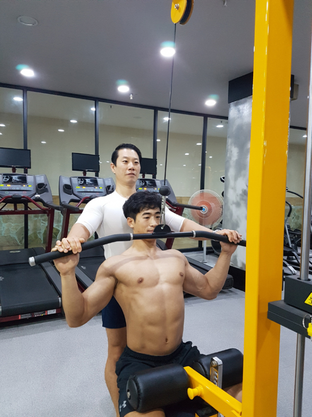 노수환 관장이 보디빌딩으로 근육이 잘 다져진 회원에게 웨이트 머신을 이용한 운동을 도와주고 있다. 태평 휘트니스 제공