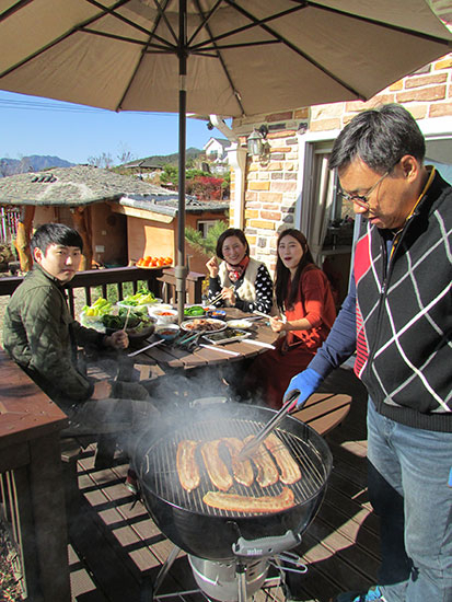 온가족이 점심 식사로 삼겹살 바베큐를 즐기고 있다.