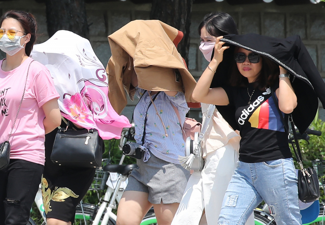 서울을 비롯한 일부 지방에 올해 들어 첫 폭염경보가 내려진 16일 오전 서울 청와대 앞을 관람온 베트남 관광객들이 따가운 햇볕을 피하기 위해 상의를 벗어 뒤집어 쓰고 걷고 있다. 연합뉴스