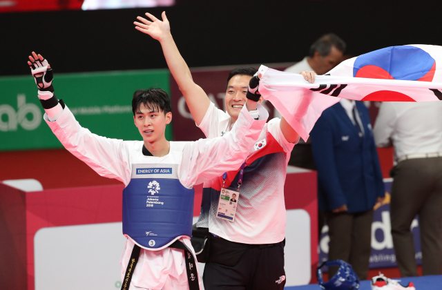 2014 인천아시안게임 금메달리스트 김태훈이 20일 인도네시아 자카르타 컨벤션센터에서 열린 태권도 남자 -58kg급 결승전에서 금메달을 획득한 뒤 코칭스태프와 함께 태극기를 들고 매트 위에서 인사하고 있다. 연합뉴스