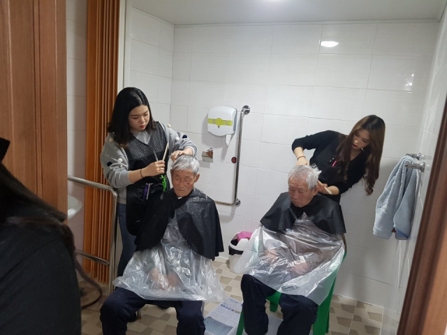 거창대학 뷰티웰니스과 재학생들이 은혜주간보호센터에 있는 어르신들의 머리를 깎고 있다.