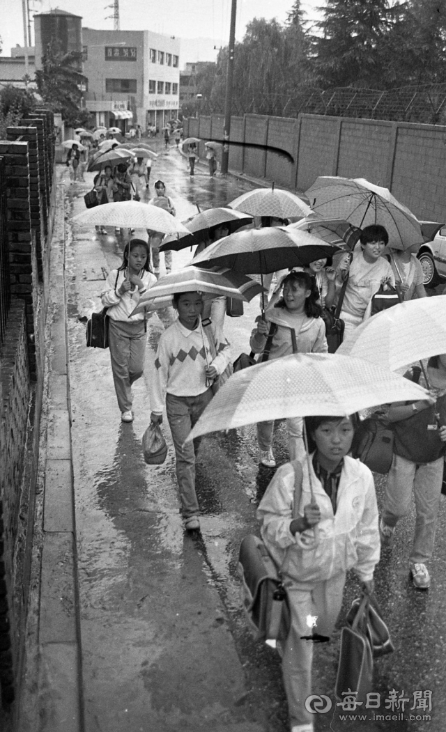 1987년 어느 날, 학생들이 우산을 쓰고 학교로 가고 있다. 철조망이 담장에 있는 곳은 옛 두류정수장이다. 매일신문 DB.