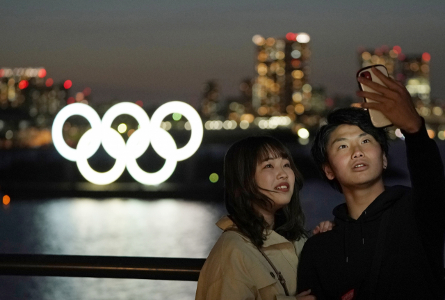 25일 일본의 남녀가 도쿄의 오다이바 해양공원에 세워진 올림픽 오륜 조형물을 배경으로 사진을 찍고 있다. EPA 연합뉴스