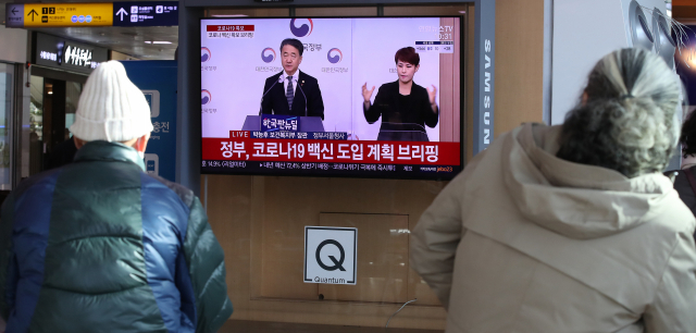 8일 서울 중구 서울역에서 시민들이 정부의 코로나19 백신 확보 브리핑을 TV화면으로 지켜보고 있다. 연합뉴스