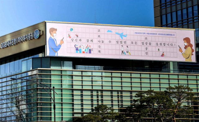 DGB대구은행이 대구 수성구 대구은행 본점 건물에 2021년 글판을 내걸고 코로나19를 극복해 나가자는 응원 메시지를 전했다. 마스크를 끼고 사회적 거리를 유지하지만, 마음만은 가까이 하자는 의미를 담아 지역민들을 위로하려는 뜻을 일러스트와 함께 표현했다. DGB대구은행 제공