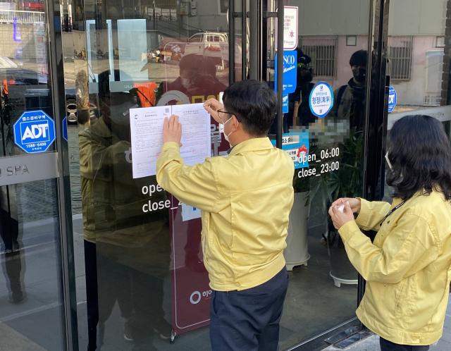 8일 오후 울산시 북구 한 사우나 건물 출입문에 시 관계자가 행정조치 45호에 따른 이용자 진단 검사와 이틀간 건물 집합 금지를 명령하는 공문을 붙이고 있다. 시는 해당 사우나에서 확진자와 접촉했던 7명이 신종 코로나바이러스 감염증(코로나19) 확진 판정을 받았다고 발표했다. 연합뉴스