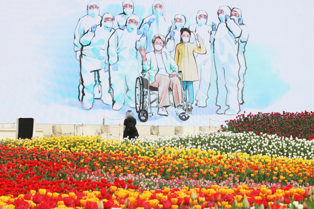 26일 오후 경기도 용인시 에버랜드에 활짝 핀 튤립 뒤로 코로나19 극복을 위해 힘쓰는 의료진에게 감사를 표하는 영상이 상영되고 있다. 연합뉴스