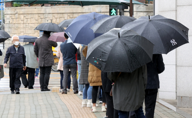12일 오후 서울 중랑구 보건소에 마련된 코로나19 임시선별진료소를 찾은 시민들이 우산을 쓰고 순서를 기다리고 있다. 연합뉴스