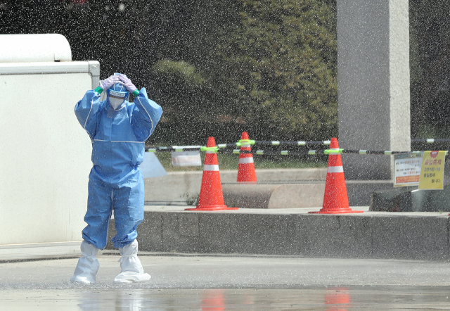10일 오후 인천시 남동구 인천문화예술회관 앞 신종 코로나바이러스 감염증(코로나19) 임시 선별검사소에서 한 방역당국 관계자가 소방대원들이 폭염 열기를 식히기 위해 뿌린 물을 맞으며 더위를 식히고 있다. 연합뉴스