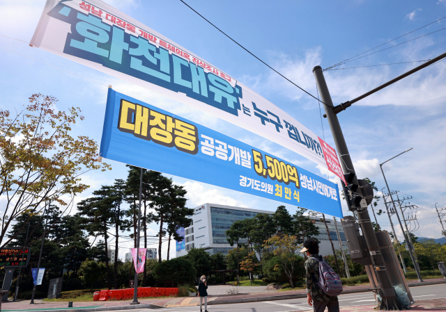 24일 경기도 성남시청 인근 교차로에 성남 대장동 개발 사업과 관련해 더불어민주당 소속 경기도의회 의원과 국민의힘 지역 당협위원장 이름으로 상반된 의미를 담은 현수막이 함께 걸려 있다. 현수막 너머로 성남시청의 모습이 보이고 있다. 연합뉴스