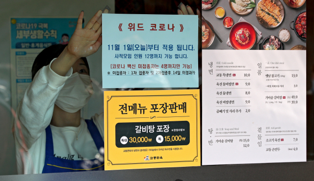 단계적 일상회복 (위드 코로나) 시행 첫날인 1일 오후 대구 중구의 한 식당 직원이 가게 유리창에 최대 12명 모임 가능 안내문을 붙이고 있다. 사진은 기사내용과 관련 없음. 김영진 기자 kyjmaeil@imaeil.com