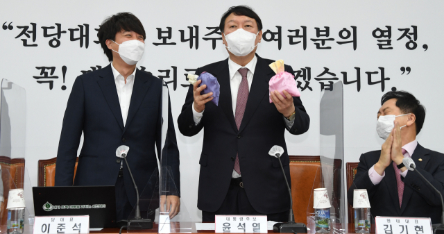 국민의힘 윤석열 대선후보(가운데)가 8일 오전 서울 여의도 국회에서 열린 최고위원회의에서 이준석 대표(왼쪽)로부터 비단주머니를 받고 발언하고 있다. 연합뉴스