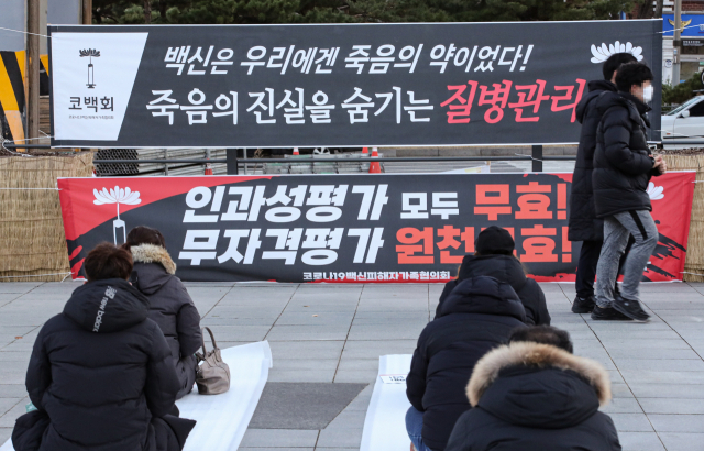 4일 오후 서울 서대문구 독립문 공원에서 코로나19 백신 접종 뒤 가족을 잃은 사람들의 모임인 코로나19 백신 피해자 가족 모임 회원들이 원인 규명과 진실을 촉구하는 집회를 열고 있다. 이 집회 참석자들이 내건 현수막 앞을 시민들이 지나가고 있다. 연합뉴스