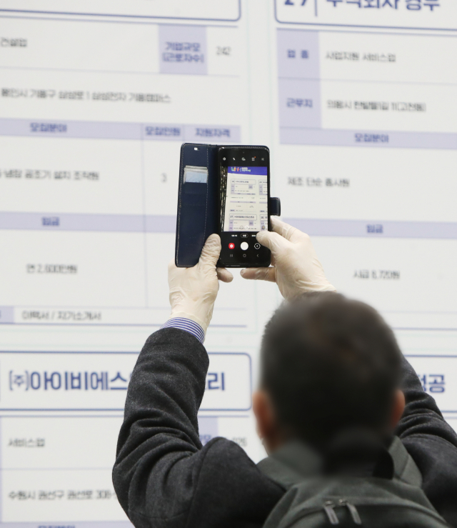 최근 한 지자체에서 열린 청년 일자리 박람회 장갑을 착용한 구직자가 채용 정보를 휴대전화로 찍고 있다. 연합뉴스