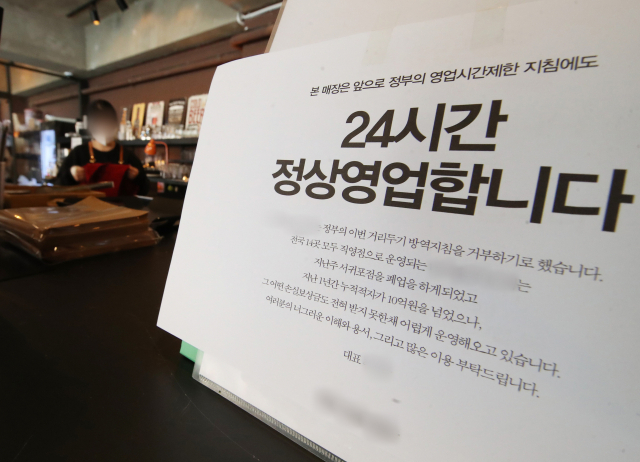 신종 코로나바이러스 감염증(코로나19) 확산으로 전국에 강화된 방역 조치가 시행 중인 21일 오후 경기도 용인의 한 카페에 정부의 영업시간 제한 조치에도 24시간 영업을 한다는 내용의 안내문이 부착돼 있다. 연합뉴스