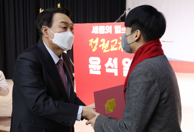 국민의힘 윤석열 대선 후보가 22일 오전 세종 비오케이아트센터에서 열린 세종 선대위 필승결의대회에서 인사말을 마친 국민의힘 제1호 청소년 당원 안상현 학생에게 빨간 목도리를 둘러주며 악수하고 있다. 연합뉴스