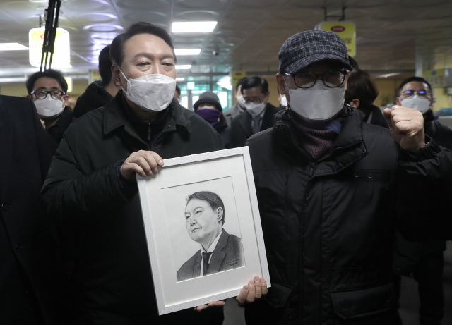 국민의힘 윤석열 대선후보가 설 명절인 1일 인천시 강화군 강화풍물시장을 방문, 지지자로부터 받은 초상화를 들어 보이고 있다. 연합뉴스