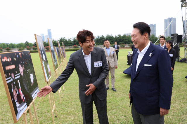 윤석열 대통령이 12일 오후 서울 용산 대통령실 청사 잔디마당에서 열린 영화관계자 초청 만찬에서 한국 배우 최초로 칸국제영화제에서 남우주연상을 수상한 배우 송강호와 사진을 보며 대화하고 있다. 연합뉴스