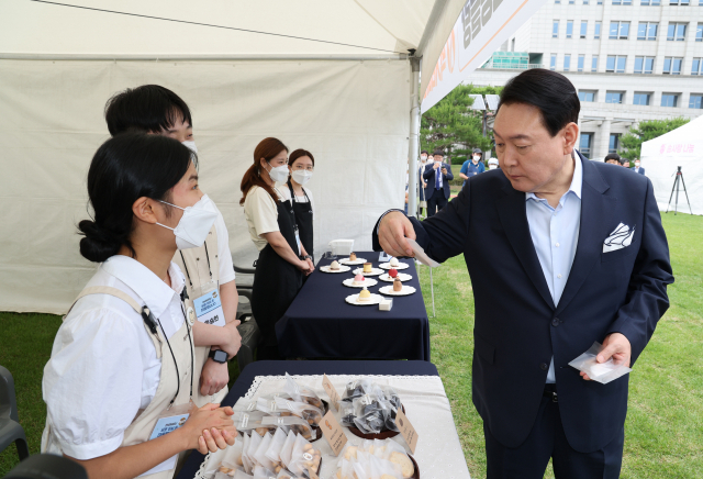 윤석열 대통령이 19일 오후 용산 대통령실 청사 앞 잔디광장에서 열린 대통령실 이전 기념 주민 초대 행사에서 용산 지역 소상공인이 참여한 먹거리 장터를 방문, 쌀과자와 브라우니 등의 제품을 살펴보고 있다. 연합뉴스