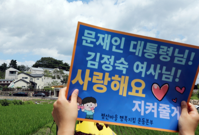 전국에서 온 문재인 전 대통령 지지자들이 17일 낮 문재인 전 대통령 사저가 있는 경남 양산시 하북면 지산리 평산마을에 모여 평산마을 평온 회복과 문 전 대통령 부부 안녕을 기원하는 집회를 했다. 한 집회 참석자가 문 전 대통령 부부를 지지하는 글이 적힌 피켓을 사저를 향해 들고 있다. 연합뉴스