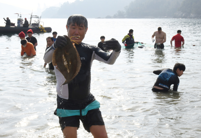 2018년 대회 후 4년만에 열린 제14회 거제도펭귄수영축제 참가자들이 경남 거제시 덕포해수욕장 겨울 바다에서 축제추진위원회가 그물을 둘러치고 풀어놓은 광어를 잡고 있다. 연합뉴스