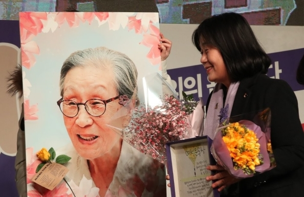2019년 3월 8일 서울 광화문광장에서 열린 제35회 한국여성대회 기념식에서 윤미향 당시 일본군성노예제문제해결을 위한 정의기억연대(정의연) 이사장이 여성운동상 수상자인 김복동 할머니 대신 수상 후 김복동 할머니의 사진을 보며 웃고 있다. 김복동 할머니는 이 시상식 개최 1개월여 전인 같은해 1월 28일 세상을 떠났다. 연합뉴스