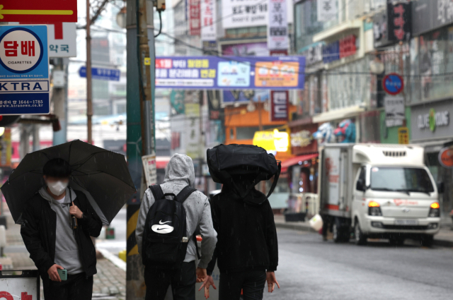 비가 내리는 19일 오전 경남 창원시 마산합포구 한 거리를 지나는 시민이 모자, 책가방 등으로 비를 피하고 있다. 연합뉴스