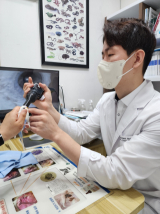 장윤호 수의사가 앵무새 외관 검사를 하고 있다. 모니터에 앵무새의 눈이 확대되어 있다.