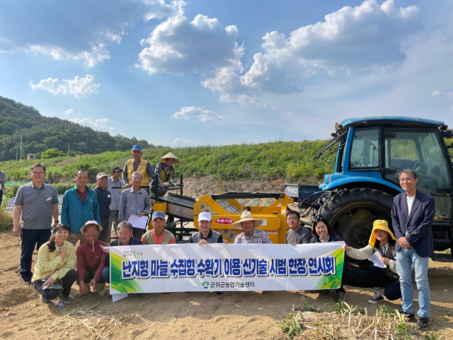 경북 군위군이 소보면 송원리 들녘에서 난지형 마늘 수집형 수확기 신기술 평가회와 기계 연시회를 열고 기념 사진을 촬영하고 있다. 군위군 제공