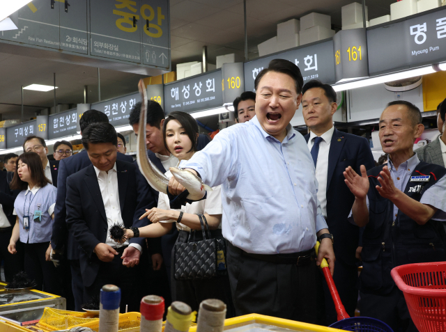 윤석열 대통령이 27일 부산 중구 자갈치시장에서 붕장어를 직접 손으로 잡아 보며 즐거워 하고 있다. 김건희 여사가 옆에서 붕장어를 잡은 윤석열 대통령을 바라보고 있다. 연합뉴스