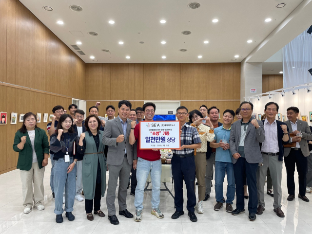 지난 26일 열린 세아메카닉스 미술동아리 전시회 오픈식에서 조창현(가운데 빨간색 티셔츠) 대표가 보다 좋은 전시환경을 조성하기 위해 새마을테마공원 측에 1천만원 상당의 조명을 기부한 뒤 기념촬영을 하고 있다. 세아메카닉스 제공