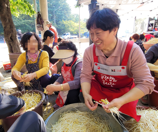 지난 12일 대구 달서구 두류공원네거리 자연보호헌장비 앞 '빨간 밥차' 봉사 현장에서 최건호(사진 오른쪽 빨간 앞치마 입은 남자) 씨가 음식 재료인 콩나물을 다듬고 있다. KT대구경북광역본부 제공.