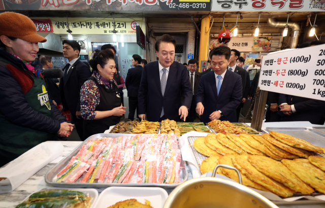 윤석열 대통령이 설 명절을 앞두고 8일 서울 광진구 중곡제일시장을 찾아 전 가게에서 박행복 사장(가운데 왼쪽) 등과 이야기하며 전을 고르고 있다. 연합뉴스