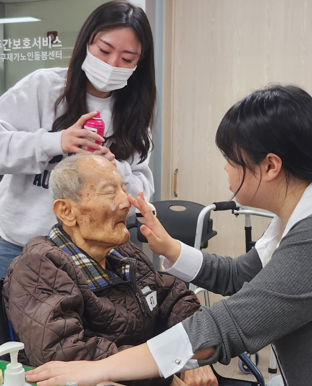 호산대 뷰티스마트케어과 학생들이 할아버지에게 장수사진을 찍기 위해 화장을 해주고 있다. 호산대 제공