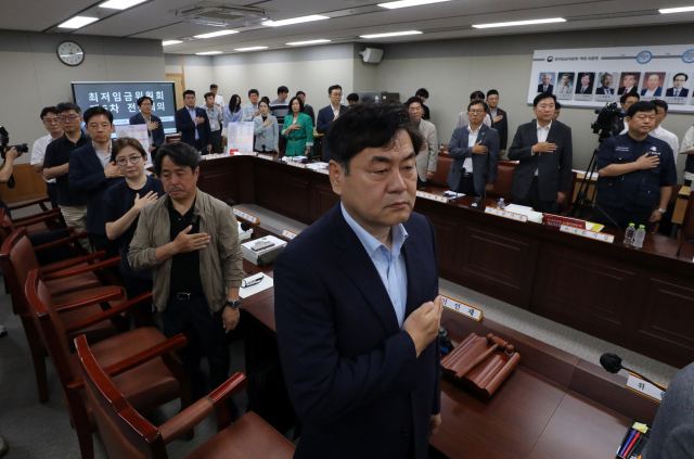 최저임금 법정 심의 기한인 27일 오후 정부세종청사 최저임금위원회에서 열린 전원회의에서 이인재 최저임금위원회 위원장을 비롯한 위원들이 국기에 경례하고 있다. 연합뉴스