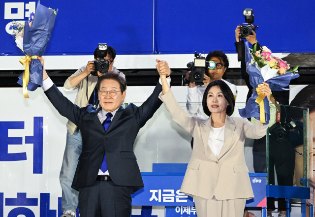 제21대 대통령 당선이 확실시되는 더불어민주당 이재명 대선 후보와 부인 김혜경 여사가 4일 서울 여의도 국회 인근에서 당 주최로 열린 국민개표방송 행사에 참석해 꽃다발을 받고서 시민들을 향해 두 팔을 들어 인사하고 있다. 연합뉴스