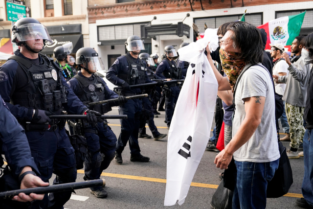 미국 로스앤젤레스(LA)에서 불법 이민자 체포와 추방에 반발하는 시위가 나흘째 이어지고 있다. 도널드 트럼프 대통령은 논란 속에 주방위군에 이어 해병대까지 투입까지 했지만 사태는 오히려 더 격렬해지고 있다. 9일(현지 시간) LA에서 불법 이민자 단속에 반대하는 한 시위 참가자가 태극기를 든 채 LA 경찰과 대치하고 있다.